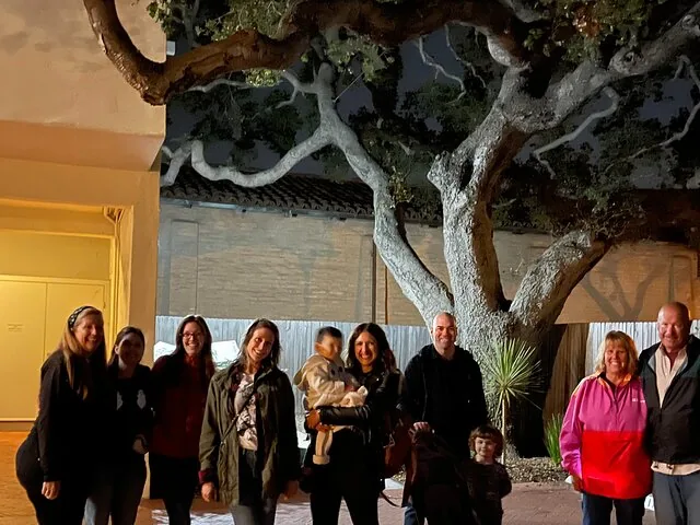 Eine Gruppe von Menschen lächelt nachts draußen in der Nähe eines großen Baumes für ein Foto.