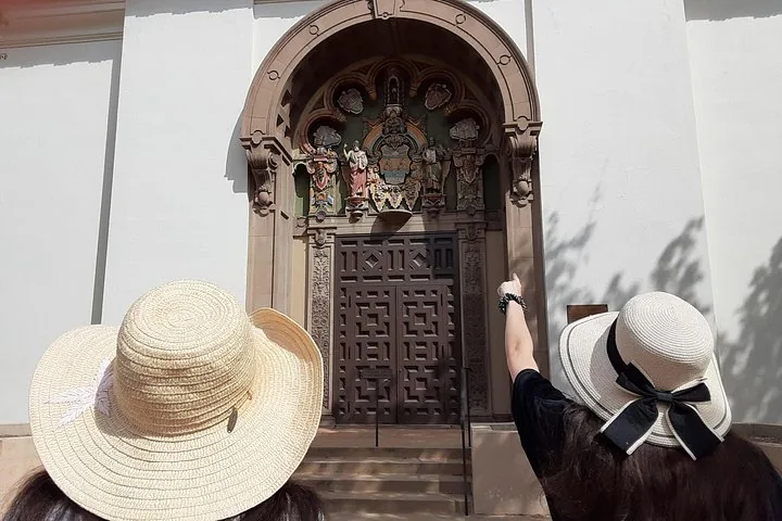 Dos mujeres con sombreros para el sol mirando una puerta adornada de un edificio.