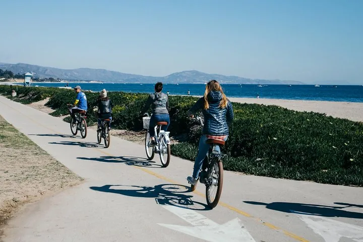 Groupe faisant du vélo électrique sur une piste cyclable pavée à côté d'une plage de sable.