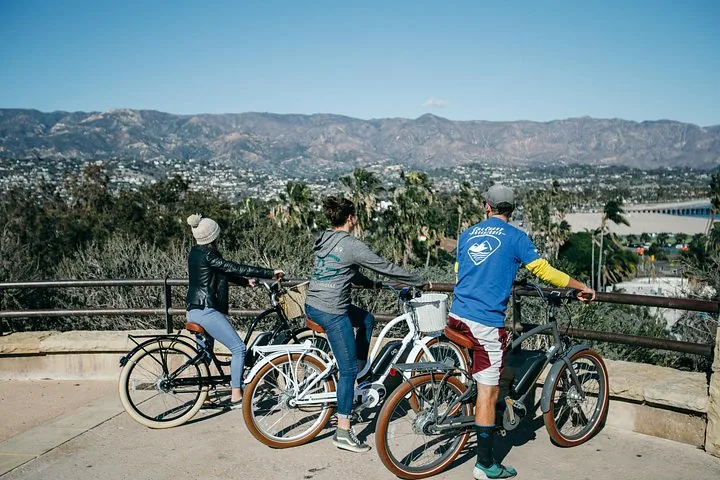 Trois personnes sur des vélos électriques admirant une vue pittoresque sur les montagnes côtières.
